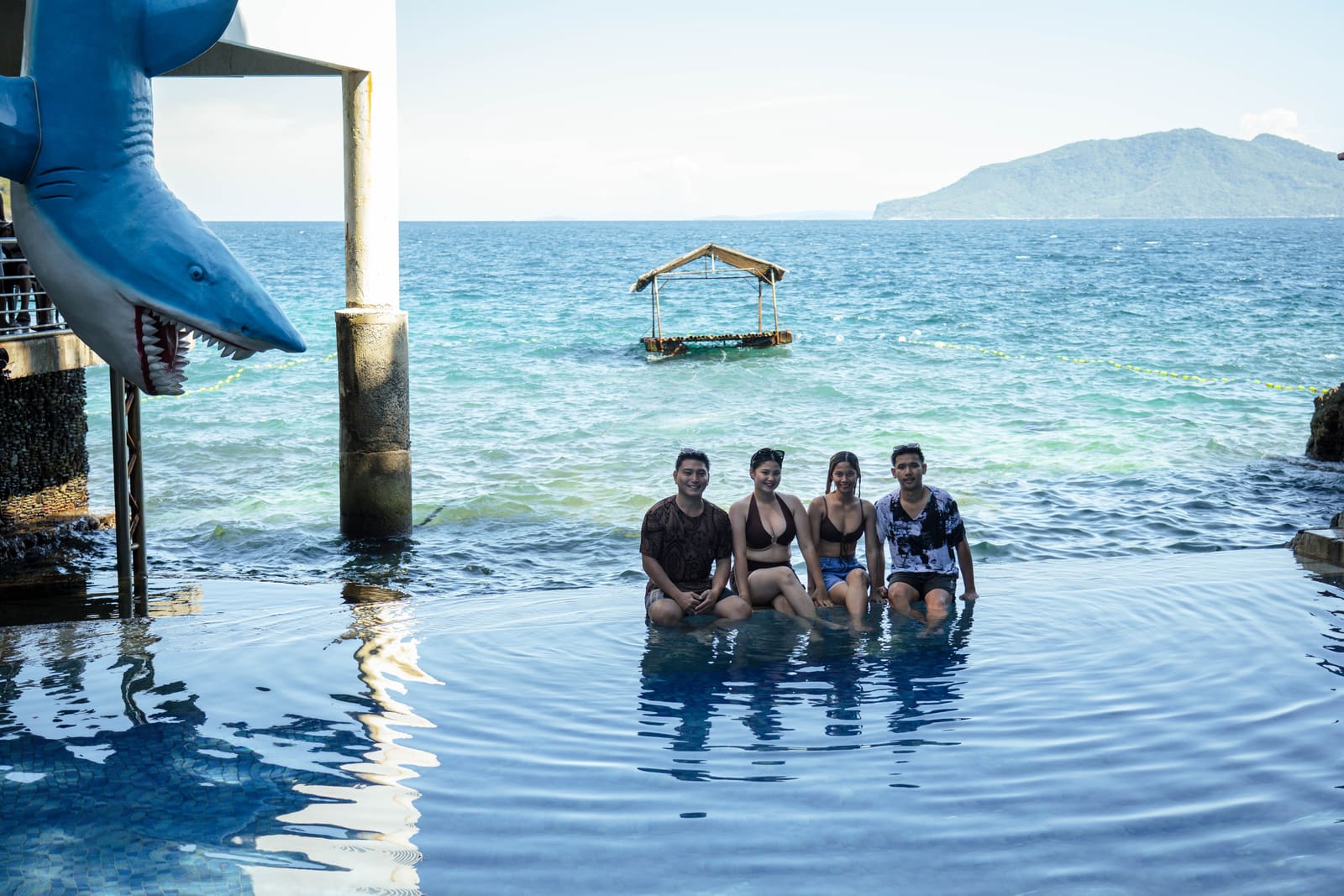 Friends sitting on the edge of the sea-view pool at Isola Vista Beach Resort, Batangas City