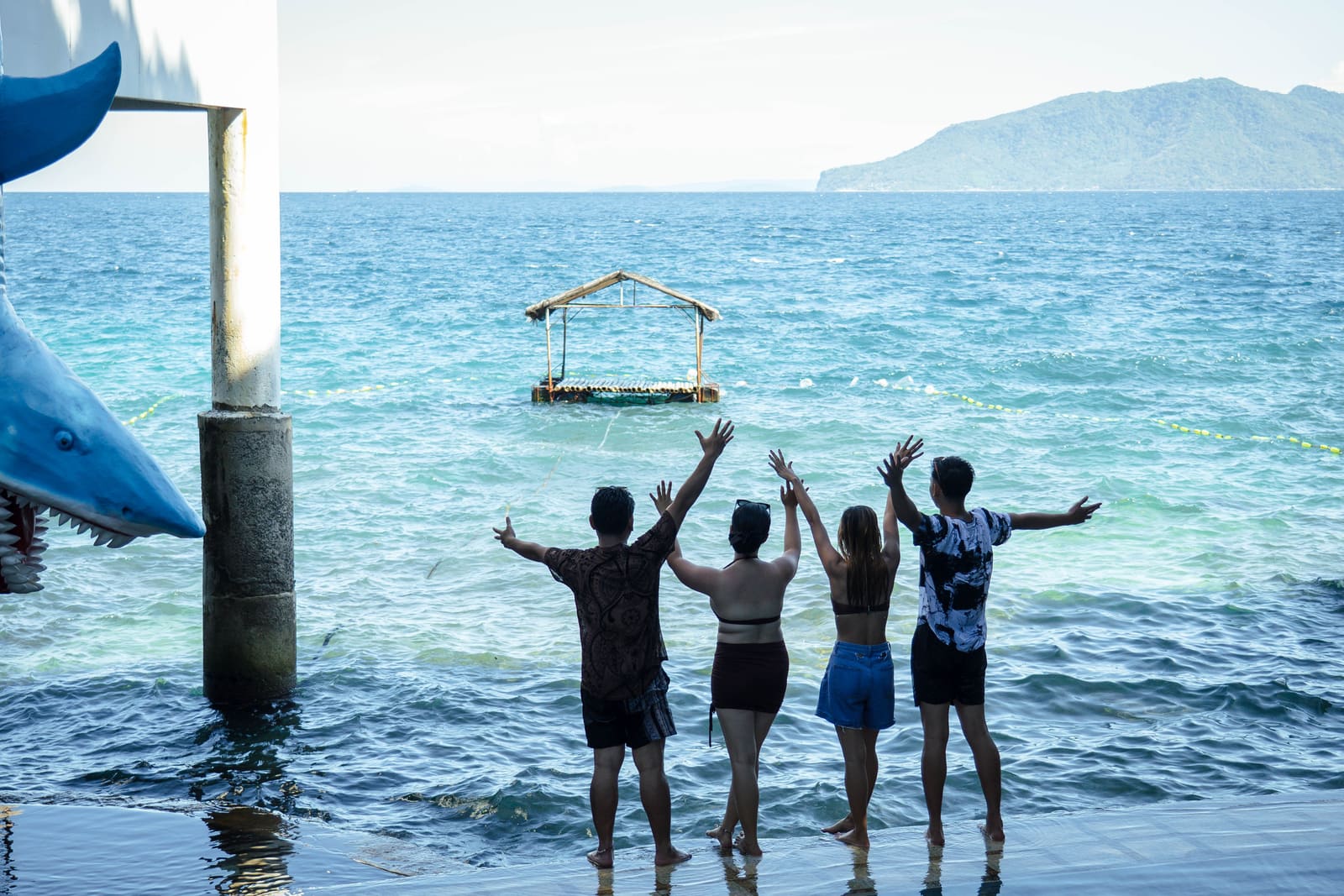 Friends waving at the sea beside the shark sculpture at Isola Vista Beach Resort, Pagkilatan